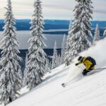 Skier descending powder run through pine trees at uncrowded Schweitzer Mountain Resort Idaho with lake views