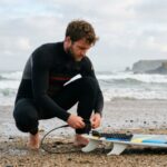 Surfer attaching an ankle leash to a shortboard before entering the ocean